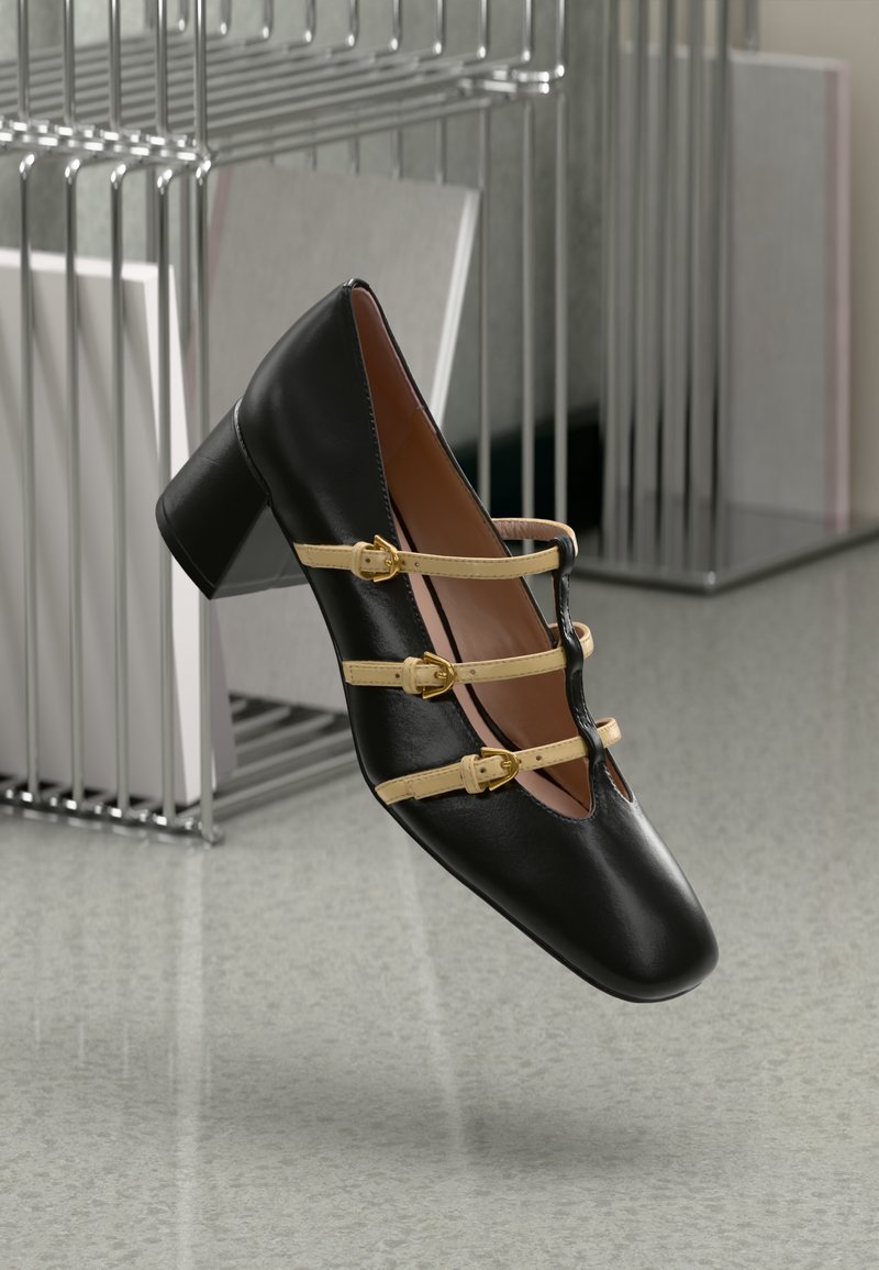 Crne kožne cipele sa kvadratnim vrhom, niskim blok petama i tri žute trake s zlatnim kopčama preko prednjeg dijela. Glatka tekstura.