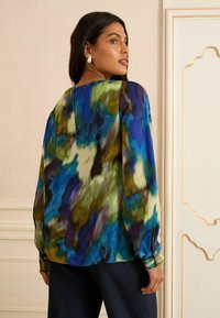 Többszínű blúz kékkel, zölddel és lilával árnyalt. Simára csiszolt anyag, ballonujjak és gombos mandzsetta hátul cipzárral.