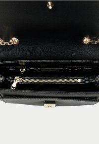 Interno di una borsa a tracolla in pelle nera con tasca con zip, hardware dorato e dettagli in catena. Finitura testurizzata. Design spazioso.