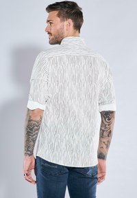 Weißes Kurzarmhemd mit vertikalen schwarzen Streifen, ausgestattet mit einer klassischen Kragen und umgeschlagenen Ärmeln, aus leichtem Stoff gefertigt.