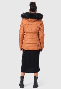 Puffer jacket in orange with a black faux fur hood and horizontal quilted design, paired with a black ribbed skirt and black boots.