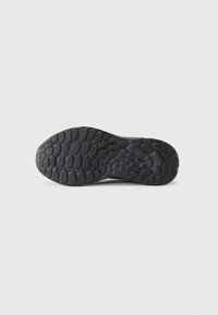 Sorte sneakersåler med en teksturert gummimønster for grep, avrundede kanter og en lett hevet midt for stabilitet.