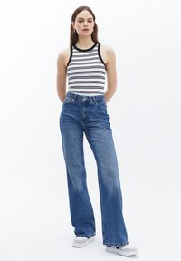 Pruhovaný bezrukávový top s černobílými pruhy, spárovaný s modrými denimovými zvonovými džínami s vysokým pasem a šedými teniskami. Jednoduchý design, neformální vzhled.