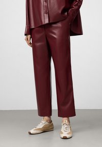 Burgunderfarbene Kunstleder-Hose mit weitem Bein, kombiniert mit beige-braunen Sneakers. Das Outfit zeichnet sich durch einen glänzenden Finish und einen lässigen Schnitt aus.