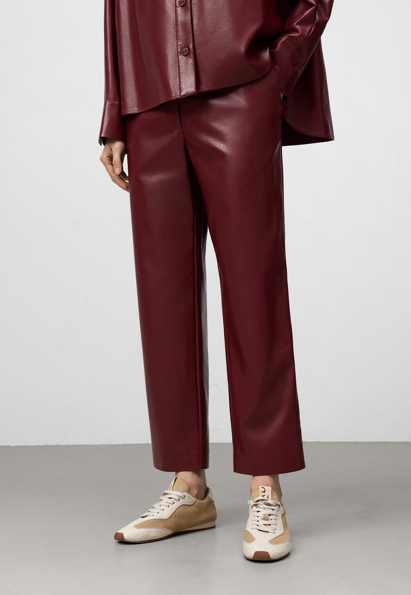 Bordeaux neplederen wijde broek in combinatie met beige en bruine sneakers. De outfit heeft een glanzende afwerking en een ontspannen pasvorm.