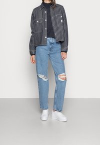 Randig denimjacka, mörkblå med vita ränder; svart tröja; ljusblå, trasiga jeans; vita platåskor.