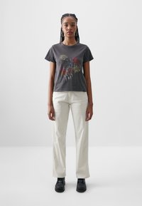 Grafisk t-shirt i mörkgrått med en panterdesign och text, kombinerad med krämfärgade vida byxor och svarta skor.