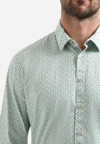 Lichtgroene overhemdd met een geometrisch patroon, klassieke kraag en witte knopen, gemaakt van zacht stof met een gladde textuur.
