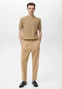 Khaki tričkové top s krátkým rukávem pletený do ribu v kombinaci se světle béžovými tailored kalhotami a černými mokasíny, zdůrazňující čisté linie a úhledný střih.