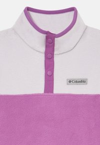 Pull en polaire blanc et violet, avec un col montant, trois boutons-pression violets et un logo Columbia sur la poitrine.