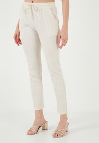 Lichte, crèmekleurige broek met een gestructureerd, verticaal gestreept patroon, elastische tailleband en zijzakken. Aansluitende, taps toelopende vorm.