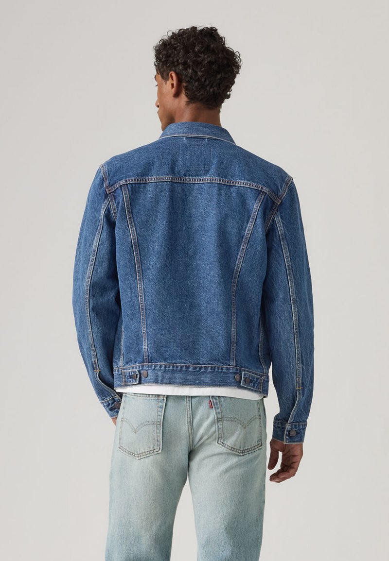 Blaue Jeansjacke mit klassischem Design, ausgestattet mit geknöpften Manschetten, Brusttaschen und hellen Ziernähten, kombiniert mit hellblauen Jeans.