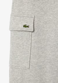 Tissu de sweat en coton gris avec une poche à rabat arborant un logo de crocodile vert. Texture lisse, design décontracté.