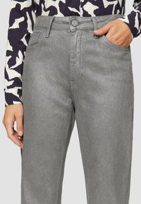 Jeans en denim métallisé argenté avec une coupe droite, dotés d'une poche avant, de passants de ceinture et d'une fermeture à bouton. Fini texturé apparent.