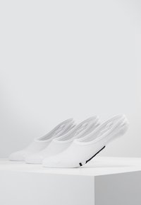 Calcetines de tobillo blancos, con un material ligero y transpirable, diseño bajo y un acento de logo negro en el lateral, exhibidos en fila.