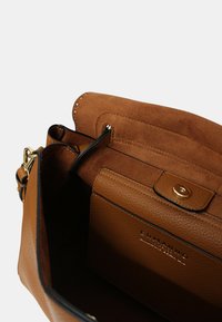 Interno di una borsa in pelle color cuoio con una morbida fodera in suede e un compartimento per carte, dotata di una chiusura a scatto e dettagli di cucitura sottili.