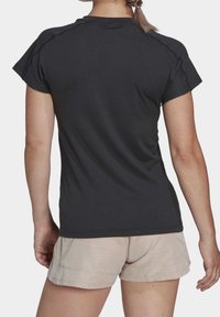 Maglietta atletica nera a maniche corte con scollo arrotondato, realizzata in un tessuto liscio e leggero, abbinata a pantaloncini beige chiaro.