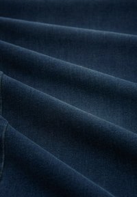 Tumedat sinised denimi kangast volditud pehmelt, ühtlaste vahedega plisseeringutega, nähtava tekstuuri ja serva äärde õmblustega.