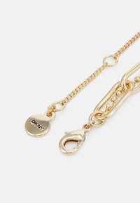 Accessoire de chaîne en or avec un fermoir et une étiquette ronde gravée "DKNY". Différents styles de maillons et une surface polie et brillante.