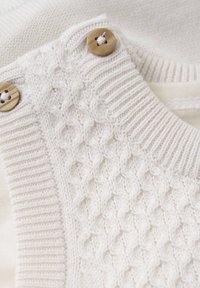 Vit stickad tröja med en texturerad mönstring, ribbad krage och två stora, knappar som accent. Mjuk tyg med en slät yta.