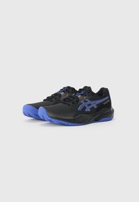 Chaussures de sport noires avec une tige lisse, des accents bleus et une semelle texturée au motif en zigzag. Conçues pour le confort et la performance.