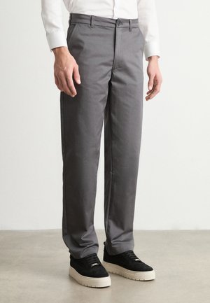 Graue Anzughosen aus gewebtem Stoff, mit geradem Bein, mittelhoher Taille und Fronttaschen. Getragen mit schwarzen Sneakers.