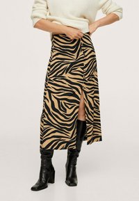Beiger Rock mit schwarzen Zebra-Streifen, mit seitlicher Schlitze und Knopfdetail. Kombiniert mit enganliegenden schwarzen kniehohen Stiefeln.