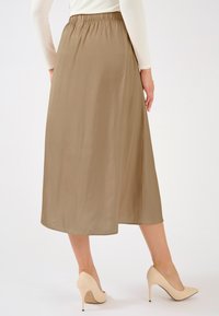 Een beige geplooide rok tot over de knie met een elastische taille, gecombineerd met naakte pumps. De rok heeft een gladde, vloeiende textuur.