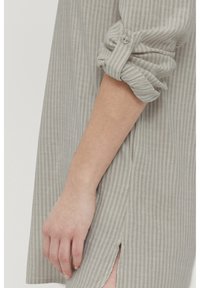 Jasnoszara koszula w paski z podwiniętymi rękawami, detalami na guzikach i bocznymi rozcięciami; wykonana z miękkiego materiału o delikatnej teksturze.