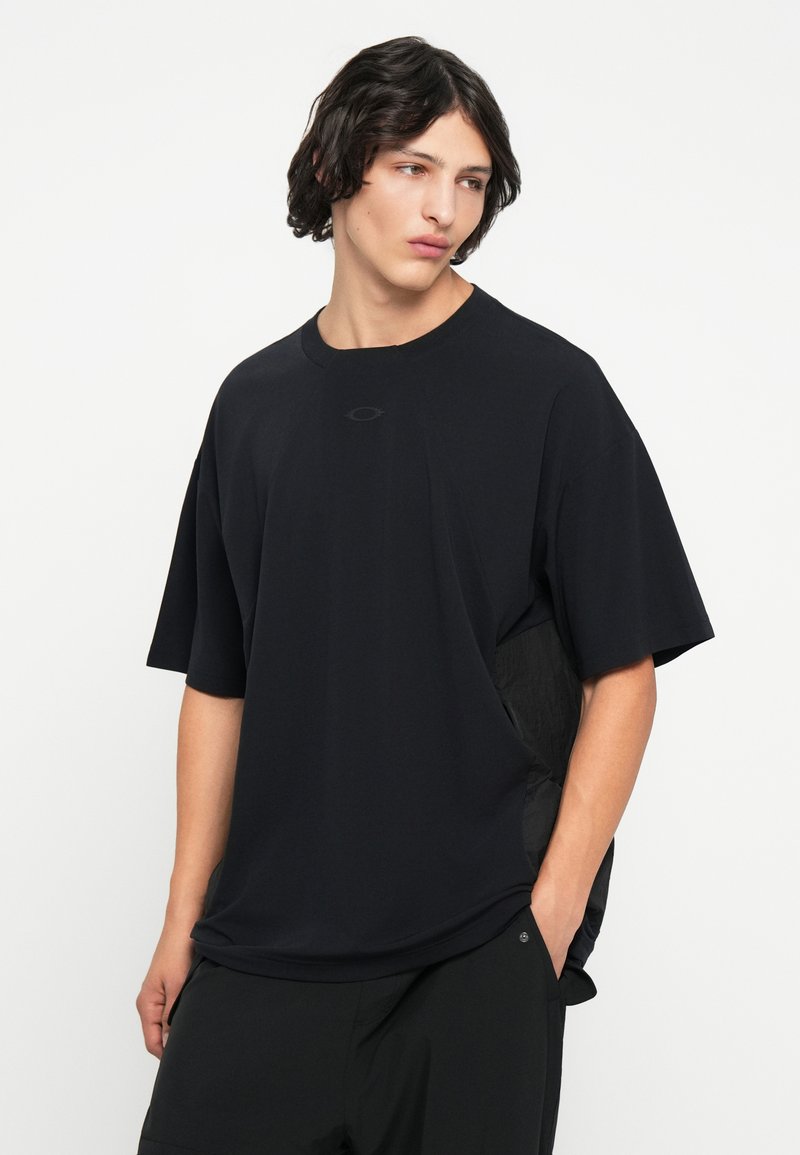 Camiseta negra de gran tamaño con mangas cortas y cuello redondo, con detalles de panel lateral texturizado. Fabricada con una tela ligera.