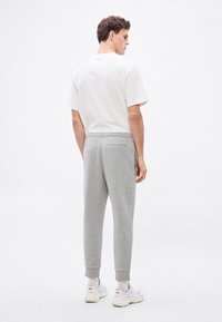 Szürke pamut melegítőnadrág szűkített szabással, bordázott szegélyekkel és hátsó zsebbel, egyszerű fehér pólóval és fehér sportcipővel párosítva.