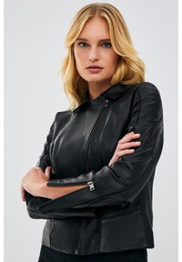 Black leather motorcycle jacket with a fitted design, zippered pockets, and an upright collar. Features textured panels and slim zippers.