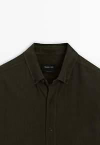 Camicia button-up verde scuro con una texture in corduroy, dotata di colletto classico e cinque bottoni frontali, realizzata in un tessuto leggero.
