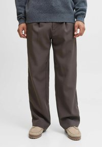 Pantalons marron à jambes larges en tissu lisse, dotés de plis avant et d'une coupe décontractée, associés à des chaussures de style mocassin beige.