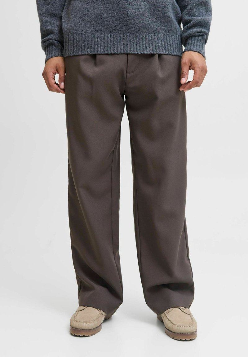 Pantalons marron à jambes larges en tissu lisse, dotés de plis avant et d'une coupe décontractée, associés à des chaussures de style mocassin beige.