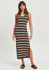 Gestreiftes Strickkleid in Schwarz, Weiß und Orange, mit V-Ausschnitt, ärmellosem Design und Schlitz an der Seite; getragen mit schwarzen Sandalen.
