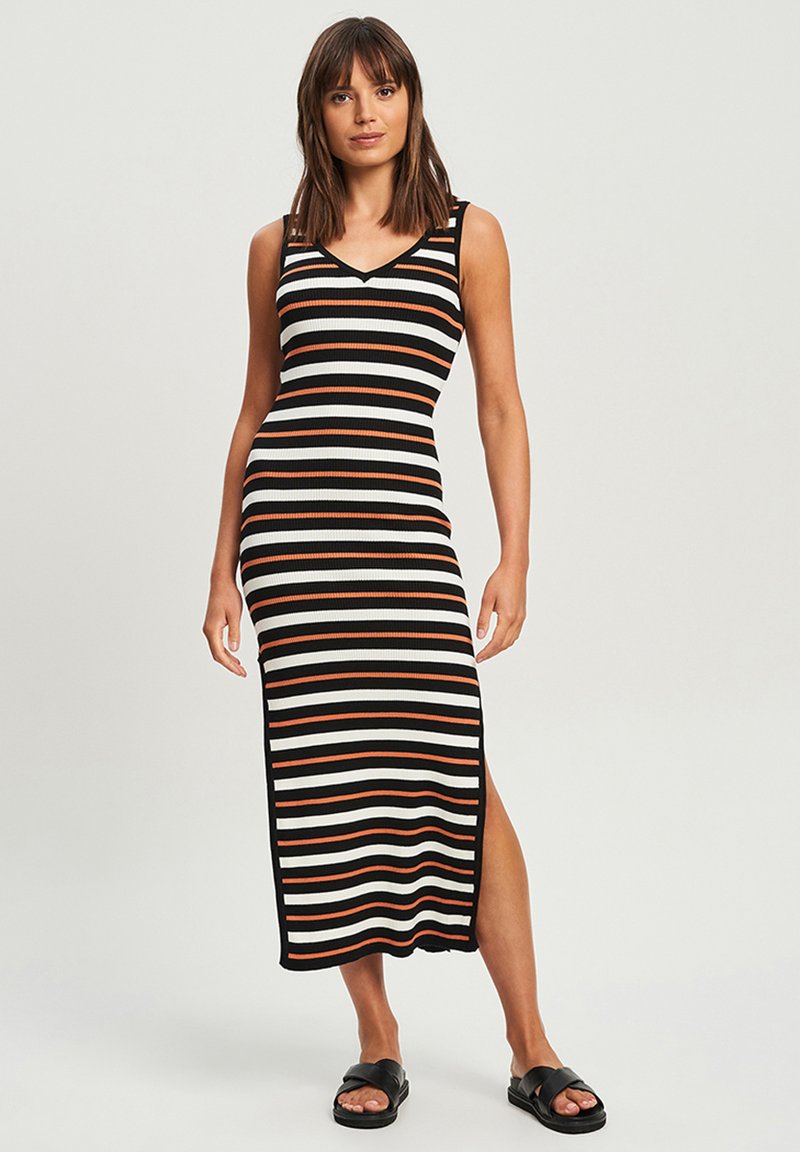 Gestreiftes Strickkleid in Schwarz, Weiß und Orange, mit V-Ausschnitt, ärmellosem Design und Schlitz an der Seite; getragen mit schwarzen Sandalen.