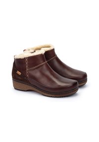 Botas de cuero marrón hasta el tobillo con un suave forro de piel crema, acentos cosidos y una suela marrón texturizada. Diseño de cuña baja para mayor comodidad.