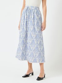 Fustă cu un model floral albastru și alb, cu talie ajustată, design fluid și material texturat. Muli negri cu toc completează look-ul.
