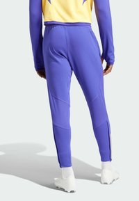 Purple athletic pants featuring a tapered design, textured material, and ankle zippers. Paired with white footwear and visible stitching details.