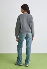 Grå crewneck sweatshirt med sänkta axlar i kombination med blå denimjeans. Har en avslappnad passform och minimalistisk design, sedd bakifrån.