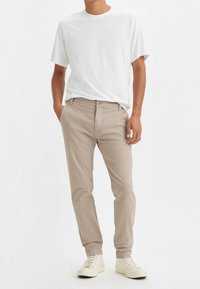 Vit kortärmad t-shirt i kombination med beige chinos, med en klassisk passform och raka ben, kompletterat med vita sneakers.