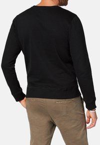 Czarny bawełniany sweatshirt z długimi rękawami, ściągaczami przy mankietach i dolnym brzegu, z okrągłym dekoltem. W połączeniu z beżowymi spodniami. Widok z tyłu.