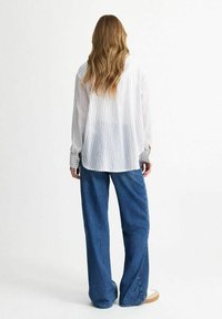 Vit skjorta med vertikala ränder och lös passform, kombinerad med vida blå denimjeans. Skjortan har långa ärmar och en rundad nederkant.