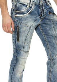 Jeans aus Denim in einem hellblauen Waschung mit ausgefransten Details. Verfügt über mehrere Taschen, Reißverschlussakzente und kontrastierende Nähmuster.