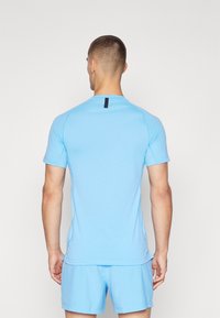 Lyseblå kortermet treningstrøye med rund hals, teksturerte sidepaneler og en svart etikett ved bakhalsen.