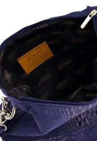 Das Innere einer lila Ledertasche mit einem Reißverschlussfach, einem geprägten Logomuster-Futter und einem tanfarbenen Lederetikett.