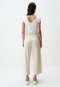 Witte top met korte mouwen en een V-vormige achterkant, gecombineerd met beige wijde broeken met een elastische tailleband en crèmekleurige instappers.