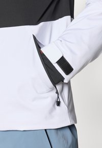 Ανδρικό αθλητικό πουλόβερ με λευκές, μαύρες και γκρίζες πάνελ; διαθέτει τσέπη με φερμουάρ, ρυθμιζόμενους καρπούς και απαλή υφή.