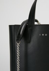 Black leather handbag with a structured design. Features a short handle and a chain accent. Silver logo detail on the side.
